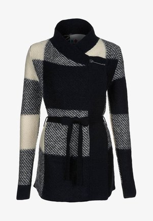 Cardigan en maille pied-de-poule noir et blanc avec col châle, taille ceinturée et fermeture par épingle de sûreté sur la poitrine.