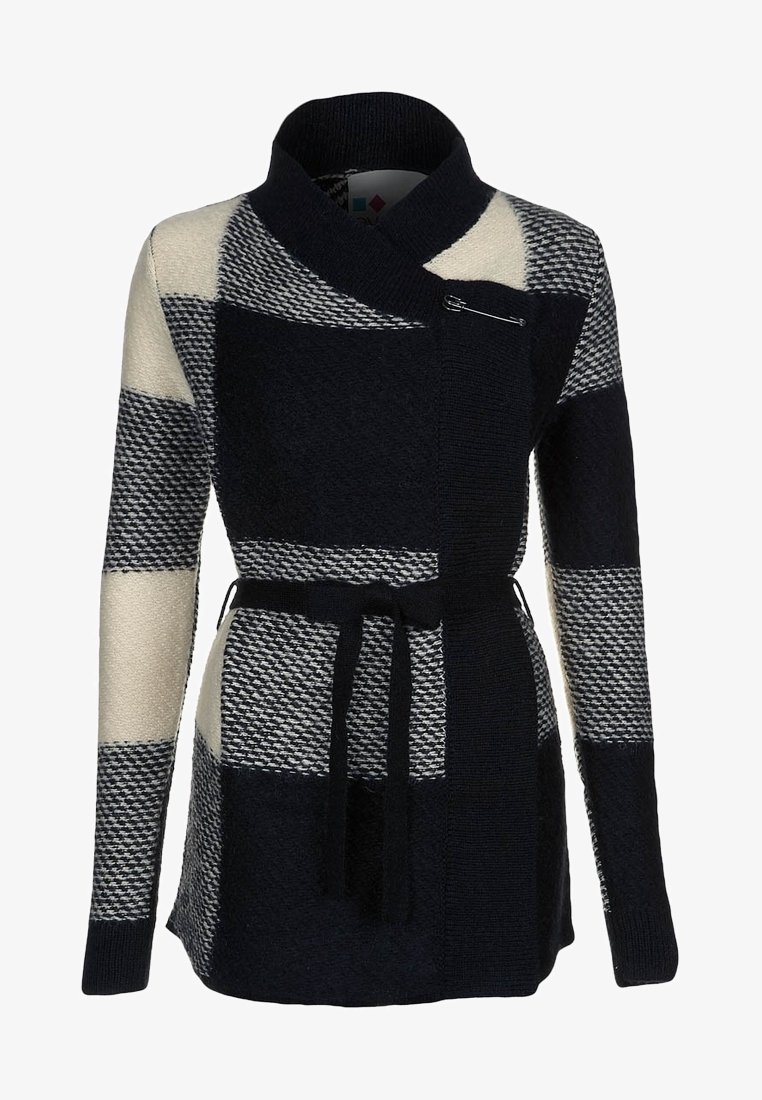 Cardigan en maille pied-de-poule noir et blanc avec col châle, taille ceinturée et fermeture par épingle de sûreté sur la poitrine.