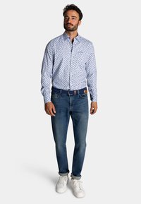 Lichtblauw overhemdsblouse met bloemmotief, gecombineerd met donkerblauwe jeans en witte sneakers. Het shirt heeft een kraag en knoopdetails.