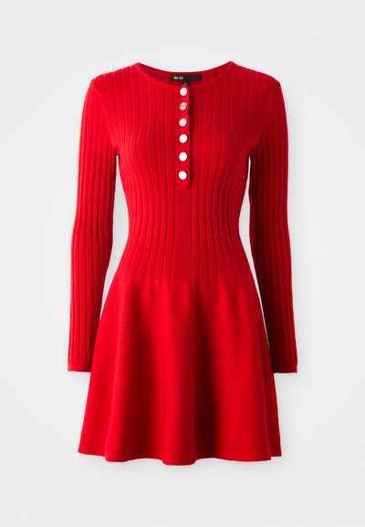 Raudonas raštuotas megztinis su ilgomis rankovėmis, prigludusia liemene ir plazdančia sijona. Hasapasta apykaklė ir penki balti mygtukai priekyje.