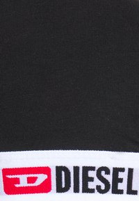 Tissu noir à rayures avec une bande blanche arborant un logo rouge et le texte "DIESEL" en noir. La texture est lisse avec un léger stretch.