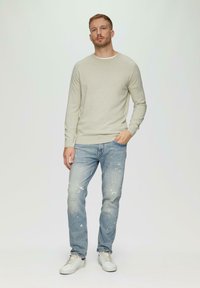 Hellgrauer Strickpullover, zerfetzte hellblaue Jeans und weiße Sneakers. Der Pullover hat lange Ärmel und einen Rundhalsausschnitt.