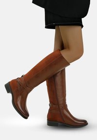 Botas marrones hasta la rodilla que presentan una combinación de texturas suaves y de ante, con punta afilada y un detalle de correa en el tobillo, además de un tacón bajo.