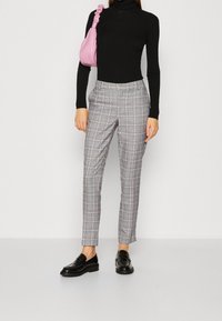 Šedé kárované kalhoty s černými, růžovými a modrými akcenty; úzký střih s bočními kapsami. Kombinované s přiléhavým černým rolákem a černými mokasínami.