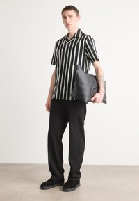 Chemise à rayures noires et vertes à manches courtes avec des boutons, associée à un pantalon noir et une pochette noire texturée. Des chaussures simples complètent le look.