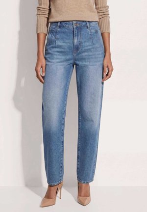 Vrouw draagt hoge taille, vervaagde blauwe rechte jeans gecombineerd met beige puntige hoge hakken en een beige geribde trui.