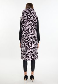 Gilet long en duvet zèbre rose et noir avec capuche, présentant un design matelassé et des poches latérales, porté sur un legging noir slim et des talons.