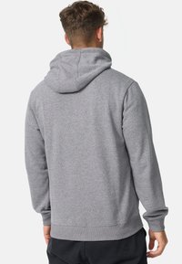 Sweat à capuche gris avec manches longues, poignets et taille côtelés. Tissu doux avec une surface texturée et capuche ajustable.