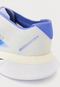 Běžecká obuv Adizero Boston 12 má bílou síťovinovou svršek s modrými akcenty, texturovanou patní část a lehkou pěnovou podrážku.