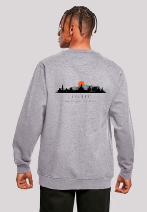 Grauer Pullover mit langen Ärmeln, der ein schwarzes Skyline-Design und eine orangefarbene Sonne zeigt. Der Text unter dem Grafik lautet „ENTFLOHEN UND DIE WELT ENTDECKEN.“