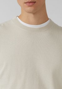 Beiger leichter Strickpullover mit Rundhalsausschnitt und Rippdetailierung. Weiche Textur, minimalistisches Design und eine figurnahe Silhouette.