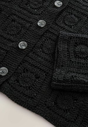 Cardigan lavorato all'uncinetto nero con motivi quadrati texturizzati e grandi bottoni rotondi grigi. Il tessuto ha una sensazione morbida e intricata.