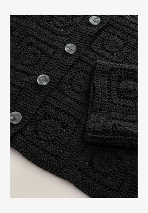 Sort hæklede cardigan med teksturerede firkantede mønstre og store runde grå knapper. Stoffet har en blød, detaljeret fornemmelse.