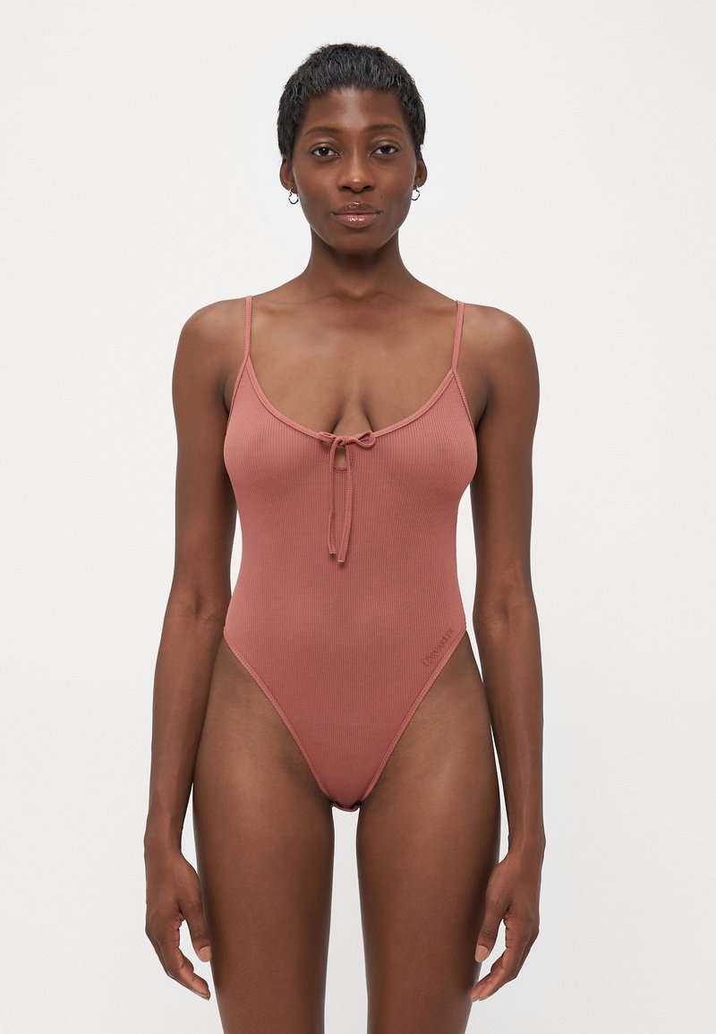 Ribbed one-piece swimsuit in dusty rose, featuring slim straps, a front tie detail, and a high-cut leg design. Subtle logo accent near hip.