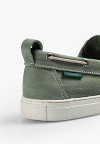 Sneaker in pelle verde con profilo basso, suola bianca con texture, cuciture a contrasto e etichetta blu con la scritta "SCALPERS" sul lato.