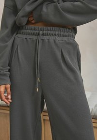 Gray waffle-textured joggers feature an elastic waistband with a drawstring, front pleats, and gold-accented aglets.