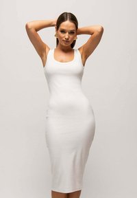 Biała, dopasowana sukienka midi z okrągłym dekoltem i ramiączkami, uszyta z gładkiego, elastycznego materiału. Podkreśla kształt sylwetki.