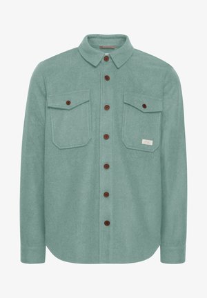 Világoskék, flanel ing, gombos gallérral, két mellzsebbel és barna gombokkal. Ívelt alsó szegéllyel és sima textúrával rendelkezik.