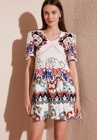 White short dress with colorful floral and geometric patterns, short puff sleeves, v-neckline, and ruffled hem. Fabric appears lightweight.