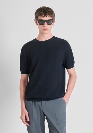Camiseta de punto texturizado de manga corta en color navy con un cuello redondo, combinada con pantalones grises y gafas de sol rectangulares oscuras.