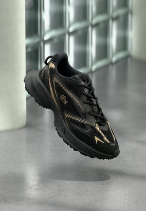 Zwarte sportschoen met ademende meshpanelen, gouden accenten en een gestructureerde zool. Voorzien van veters, een afgeronde neus en een dempend ontwerp.