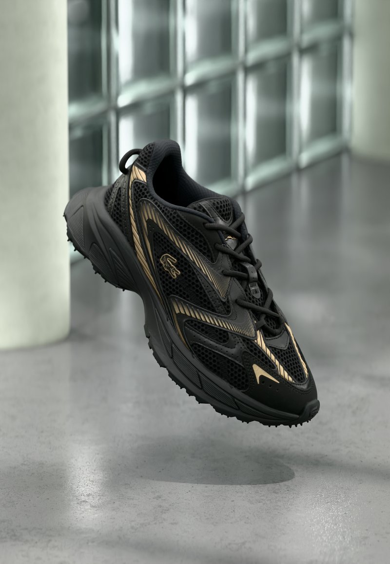 Μαύρο αθλητικό παπούτσι με πλέγμα, χρυσές λεπτομέρειες και υφασμένο πέλμα. Διαθέτει κορδόνια, στρογγυλεμένη μύτη και μαλακό, άνετο σχεδιασμό.