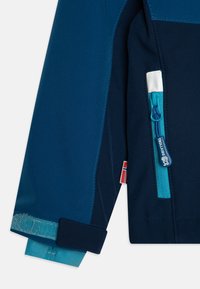 Giacca blu navy con tasca con zip e accenti turchesi, tessuto testurizzato e polsini regolabili con fascia in velcro.