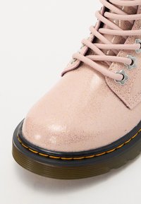 Bota de tobillo rosa brillante con punta redondeada, parte superior de cuero estampado, cordones rosa, ojales plateados y una suela de goma negra con costuras amarillas.