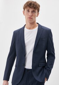 Navy blue blazer with a textured fabric, single button closure, two front pockets, and a notch lapel, paired with a white crew neck t-shirt.