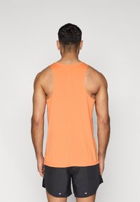 Πορτοκαλί αμάνικη μπλούζα από ελαφρύ ύφασμα, με σχέδιο racerback και ίσιο τελείωμα, συνδυασμένη με μαύρο αθλητικό σορτς.