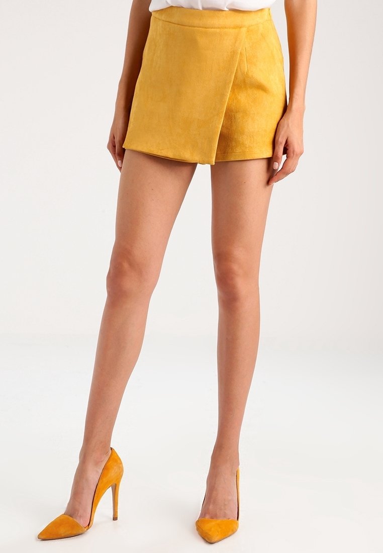Gul nubuckminikjol med en asymmetrisk design. Kombinerad med matchande gula högklackade skor som framhäver en smidig silhuett.