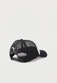 Μαύρο και άσπρο δίχτυ καπέλο τύπου trucker με ρυθμιζόμενο snapback και λογότυπο Puma στο πίσω μέρος, τοποθετημένο σε λευκή επιφάνεια.