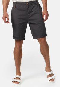 Shorts en coton gris avec détail de bouton, revers roulés et poches latérales, assortis à des sandales blanches. Texture lisse, coupe décontractée.