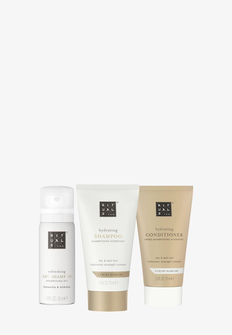 Three hair care products: a white cylindrical bottle for dry shampoo, and two tubes for hydrating shampoo and conditioner, in white and gold.