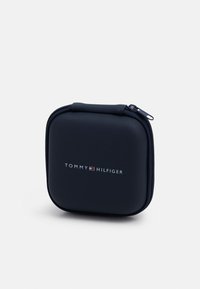 Custodia rigida blu navy con chiusura a zip, caratterizzata da un esterno testurizzato e un logo argentato sulla parte anteriore. Design compatto e di forma quadrata.