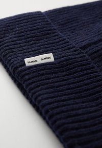 Navy ribbed knit beanie with a soft texture, featuring a white fabric label with "SAMØE SAMSØE" printed in black.