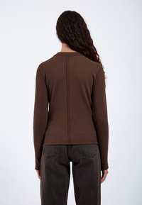 Brown fitted long-sleeve top with a textured, ribbed design and a back seam detail. Paired with high-waisted dark jeans.