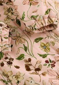 Tela con estampado floral en un suave tono rosa. Presenta un material texturizado y acanalado con diseños florales verdes y marrones, acentuados por bordes recogidos.