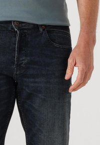 Donkerblauwe denim jeans met een slim fit, voorzien van vijf zakken, een zichtbare knoop- en ritssluiting, en subtiele vervaging in de stof.