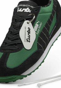Baskets noires et vertes avec des matériaux en mesh et en suède, accents blancs, semelle en caoutchouc, et une étiquette suspendue portant "Porsche turbo" et "PUMA Easy Rider."