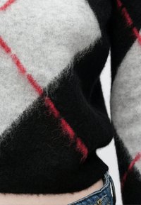 Črno, sivo in rdeče karo pleten pulover. Mehka tekstura z izrazitim diagonalnim vzorcem; prilegajoč se kroj okoli pasu, priložnostni slog.