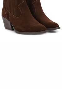 Botas western de ante marrón con punta afilada y tacón bajo apilado, que presentan acentos acanalados en el eje para mayor textura.