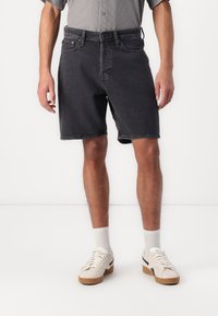 Svarta denimshorts med vanlig passform, med fem fickor, bälteshål och en lätt blekt finish. Matchas med vita sneakers och strumpor.