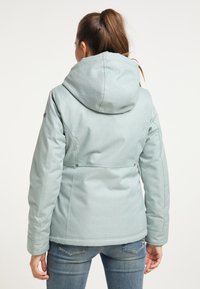 Chaqueta azul claro con capucha, confeccionada en tela texturizada. Presenta un diseño ajustado, costuras laterales y cierres de presión en la cintura.
