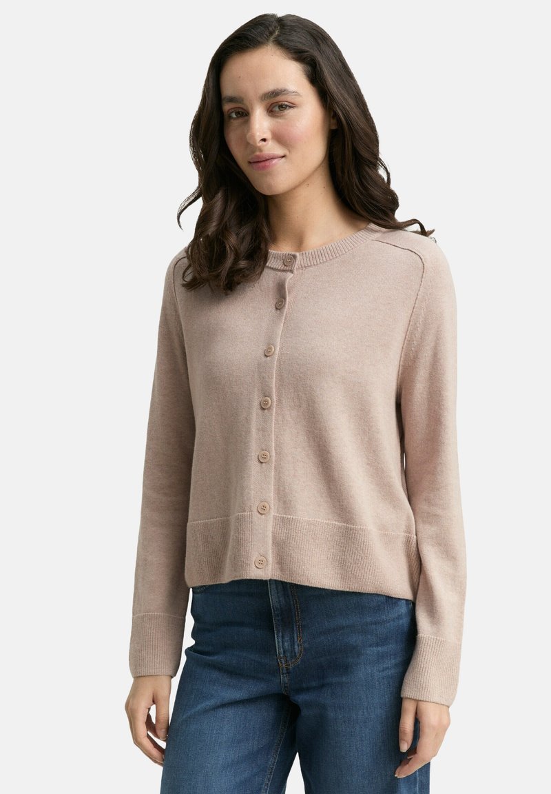 Lichtroze cardigan van zachte stof, met een ronde halslijn, knoopsluiting en ribgebreide zoom en manchetten. Gemaakt in combinatie met blauwe jeans.
