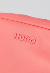 Torba od tkanine s koraljnim teksturom s ugraviranim logotipom "HUGO" u usklađenoj boji. Jednostavan dizajn s glatkom površinom i bez dodatnih metalnih elemenata.