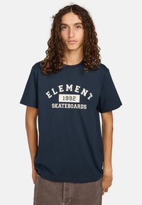 Námořnická modrá bavlněná tričko s nápisem "ELEMENT 1992 SKATEBOARDS" v bílé barvě, klasický kulatý výstřih a krátké rukávy. Měkká textura.