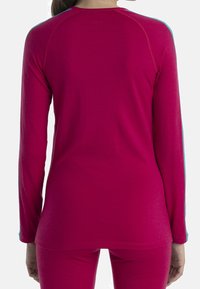 Långärmad topp i fuchsia med figurnära design, kontrasterande blå detaljer vid axlarna och mjukt material. Rundad nederkant och stretchigt material.