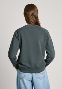 Mörkgrå sweatshirt med klassisk rund hals och raglanärmar. Mjuk textur, ribbade ärmslut och midja. Bärs med ljusblå jeans.