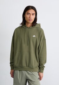 Ελιά πράσινη φούτερ φτιαγμένο από μαλακό ύφασμα, διαθέτει τσέπη καγκουρό, κουκούλα με κορδόνια και λευκ�ό λογότυπο Nike στο στήθος.